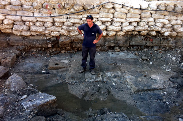 A member of the Israel Antiquities Authority standing on the ancient quay that was exposed at Akko. In the middle of the picture one can see the floor of the quay, built of large dressed stones. In some of the stones there is a hole for inserting a wooden pole – probably for mooring and/or dragging the boat (the Israel Antiquities Authority)