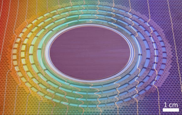 Heat cloak: a series of concentric rings lets heat propagating from left to right across a metallic sheet flow more readily around a thermally isolated disk than toward its center, leaving no sign of the disk in the temperature distribution on the right side; the colors represent temperatures measured with an infrared camera and are superimposed on a photo of the structure before the rubbery insulating material was added to the holes and gaps; the white lines connect points at the same temperature (R. Schittny / KIT)