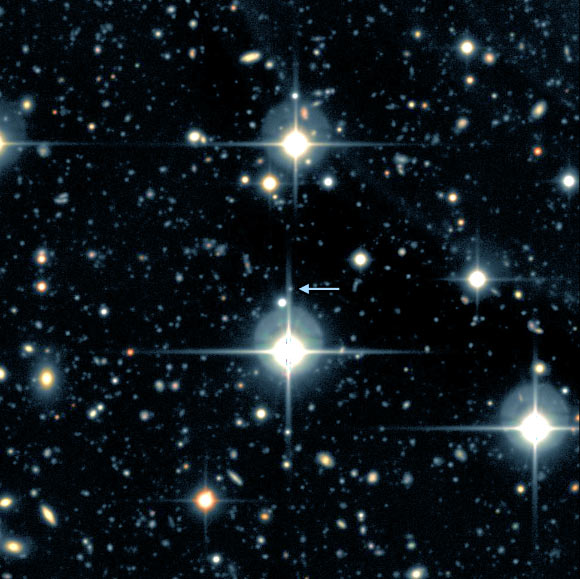 This image shows the supernova SNLS-06D4eu and its host galaxy, arrow. The supernova and its host galaxy are so far away that both are a tiny point of light that cannot be clearly differentiated in this image. The large, bright objects with spikes are stars in our own galaxy. Every other point of light is a distant galaxy. Image credit: University of California, Santa Barbara.