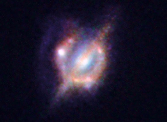 H-ATLAS J142935.3-002836, an object seen by the Hubble Space Telescope and the Keck-II telescope on Hawaii with the help of a gravitational lens. In this image one can see the foreground galaxy that is doing the lensing, which resembles how our Milky Way Galaxy would appear if seen edge-on; but around this galaxy there is an almost complete ring - the smeared out image of a star-forming galaxy merger far beyond. Image credit: ESO / NASA / ESA / W. M. Keck Observatory.