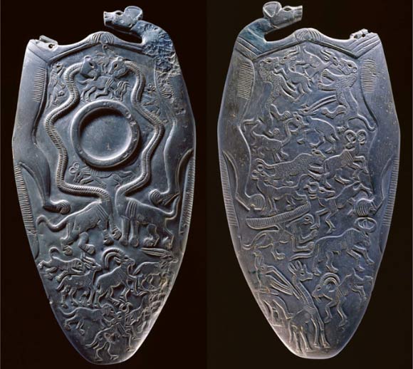 The obverse and reverse surfaces of a 5,150-year-old siltstone ceremonial palette discovered at Hierakonpolis, Egypt. The object is surmounted and framed by two wild dogs (Lycaon pictus) clasping one another’s paws; other species include ostrich, hartebeest, wildebeest, ibex, oryx, and giraffe; some fictitious animals are also depicted, including serpent-necked panthers, or ‘serpopards,’ and a plausible griffin. Image credit: Ashmolean Museum.
