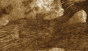 The moons of our Solar System are brimming with unusual landscapes. However, sometimes they look a little more familiar, as in this new radar image from the Cassini orbiter. The image shows dark streaks carved into dunes reminiscent of those we might find on a beach on Earth, or raked with flowing lines in a Japanese Zen garden — but this scene is actually taking place on Saturn’s moon Titan. While our sand is composed of silicates, the ‘sand’ of these alien dunes is formed from grains of organic materials about the same size as particles of our beach sand. The small size and smoothness of these grains means that the flowing lines carved into the dunes show up as dark to the human eye. While previous images have spotted these eerily familiar patterns on Titan's dunes, this new image (colorized) shows them in greater detail. The image was obtained by Cassini's radar mapper on July 10, 2013. The vertical seam near the center is an artifact of radar image data processing. Image credit: NASA / JPL-Caltech / Sci-News.com.