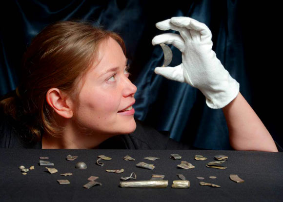 Archaeologist examines a crescent shaped brooch fragment from the Aberdeenshire hoard. Image credit: © Phil Wilkinson / University of Aberdeen.