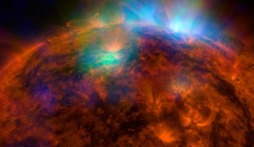 X-rays stream off the Sun in this image. The NuSTAR data, seen in green and blue, reveal solar high-energy emission (green shows energies between 2 and 3 kiloelectron volts, and blue shows energies between 3 and 5 kiloelectron volts). The high-energy X-rays come from gas heated to above 3 million degrees. The red channel represents UV light captured by SDO at wavelengths of 171 angstroms, and shows the presence of lower-temperature material in the solar atmosphere at 1 million degrees. This image shows that some of the hotter emission tracked by NuSTAR is coming from different locations in the active regions and the coronal loops than the cooler emission shown in the SDO image. Image credit: NASA / JPL-Caltech / GSFC.