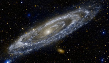 Hot stars burn brightly in this image from NASA's Galaxy Evolution Explorer, showing the UV side of a familiar face. At 2.5 million light-years away, the Andromeda galaxy is our Milky Way's largest galactic neighbor. The galaxy spans 260,000 light-years across. The bands of blue-white making up the galaxy's striking rings are neighborhoods that harbor hot, young, massive stars. Dark blue-grey lanes of cooler dust show up starkly against these bright rings, tracing the regions where star formation is currently taking place in dense cloudy cocoons. Eventually, these dusty lanes will be blown away by strong stellar winds, as the forming stars ignite nuclear fusion in their cores. Meanwhile, the central orange-white ball reveals a congregation of cooler, old stars that formed long ago. When observed in visible light, the galaxy’s rings look more like spiral arms. The UV image shows that these arms more closely resemble the ring-like structure previously observed in infrared wavelengths with NASA’s Spitzer Space Telescope; astronomers interpreted these rings as evidence that the galaxy was involved in a direct collision with its neighbor, Messier 32, more than 200 million years ago. Image credit: NASA / JPL-Caltech.