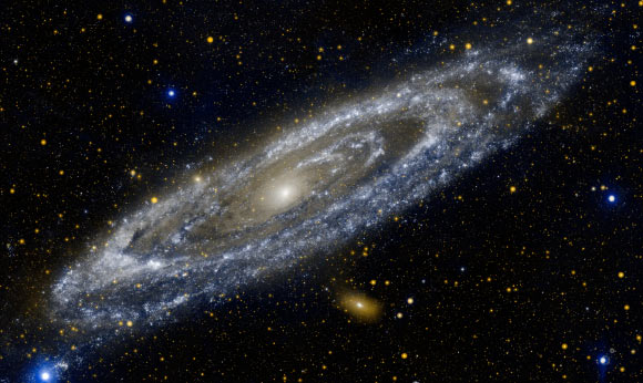 Hot stars burn brightly in this image from NASA’s Galaxy Evolution Explorer, showing the UV side of a familiar face. At 2.5 million light-years away, the Andromeda galaxy is our Milky Way’s largest galactic neighbor. The bands of blue-white making up the galaxy’s striking rings are neighborhoods that harbor hot, young, massive stars. Dark blue-grey lanes of cooler dust show up starkly against these bright rings, tracing the regions where star formation is currently taking place in dense cloudy cocoons. Eventually, these dusty lanes will be blown away by strong stellar winds, as the forming stars ignite nuclear fusion in their cores. Meanwhile, the central orange-white ball reveals a congregation of cooler, old stars that formed long ago. When observed in visible light, the galaxy’s rings look more like spiral arms. Image credit: NASA / JPL-Caltech.