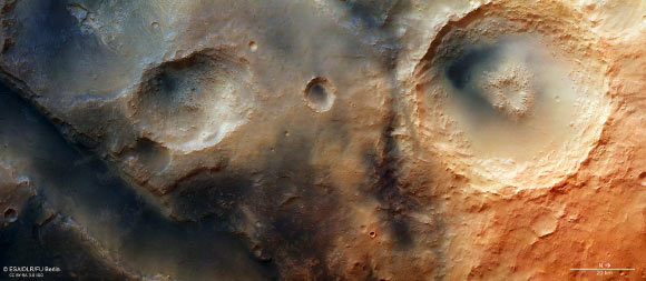 The Nili Fossae system, part of which is shown in this image, is an area of great geological interest near the giant Isidis impact basin, northeast of the Syrtis Major volcanic province. The system contains numerous troughs, one of which can be seen crossing the lower left of this image. On the plateau above, several depressions can be seen, some of them extending into the trough. A large, 55 km-diameter impact crater with a central pit can be seen on the right. This image was acquired by the High Resolution Stereo Camera on the Mars Express on 16 October 2014. North is to the right, east is up. Image credit: ESA / DLR / FU Berlin / CC BY-SA 3.0 IGO.
