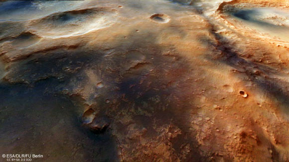 Nili Fossae is characterised by its semi-circular curve around the edge of the impact basin, which implies that these are rifts that occurred as a result of tensile stress caused by settlement in the Martian crust following the Isidis impact. When the multi-kilometer deep basin was pushed downwards even further by the load of massive, iron-rich lava deposits, the edge of the crater was subjected to severe tensile stress and the crust cracked. This oblique perspective view of Nili Fossae was generated using data from the stereo channels. Image credit: ESA / DLR / FU Berlin / CC BY-SA 3.0 IGO.