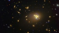 This image shows Abell 3827, a massive galaxy cluster approximately 1.3 billion light years away. The blue structures surrounding the central galaxies are gravitationally lensed views of a much more distant galaxy behind the cluster. Observations of the central four merging galaxies have provided hints that the dark matter around one of the galaxies is not moving with the galaxy itself, possibly implying dark matter-dark matter interactions of an unknown nature are occurring. Image credit: ESO.
