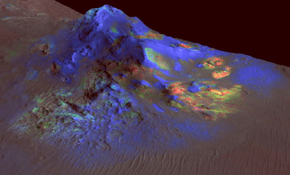 Deposits of impact glass have been preserved in Martian craters, including Alga Crater, shown here. In color coding based on analysis of data from the CRISM instrument on NASA’s Mars Reconnaissance Orbiter, green indicates the presence of glass; blues are pyroxene; reds are olivine. This view shows Alga Crater’s central peak, which is about 3 miles (5 km) wide within the 12-mile (19-km) diameter of this southern-hemisphere crater. The information from CRISM is shown over a terrain model and image based on observations by the High Resolution Imaging Science Experiment (HiRISE) camera. The vertical dimension is exaggerated by a factor of two. Image credit: NASA / JPL-Caltech / JHUAPL / University of Arizona.