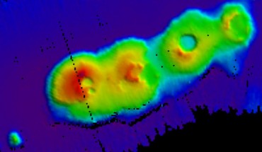 A 3D relief map of the volcanic cluster on the sea floor. The sea floor is represented by a dark blue color and there are four calderas rising out of the sea floor in shades of green, yellow, orange and red. Image credit: University of New South Wales.