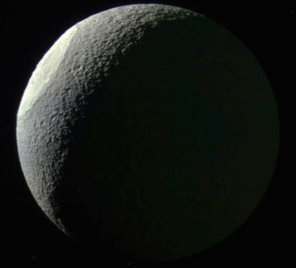This image of Tethys was snapped on May 9, 2015 from a distance of 186,000 miles (300,000 km) from the moon. The moon’s dark side is faintly illuminated by reflected light from Saturn. North on Tethys is up in this view. The impact crater Odysseus is seen at the left. Image credit: NASA / JPL-Caltech / Space Science Institute.