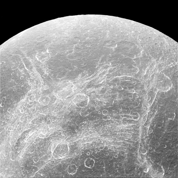 This image from NASA’s Cassini spacecraft shows a part of Dione’s surface that is covered by linear, curving features, called chasmata. The Voyager spacecrafts observed Dione in 1980 showing a complex surface structure, with wispy features on its trailing hemisphere. The nature of these features was unclear until 2004, when the Cassini spacecraft showed that they weren’t surface deposits of frost, as some had suspected, but rather a pattern of bright icy cliffs among myriad fractures. One possibility is that this stress pattern may be related to Dione’s orbital evolution and the effect of tidal stresses over time. This view looks toward the trailing hemisphere of Dione. Cassini obtained the image with its narrow-angle camera on April 11, 2015. The view was acquired at a distance of 68,000 miles (110,000 km) from Dione. North on Dione is up. Image credit: NASA / JPL-Caltech / Space Science Institute.