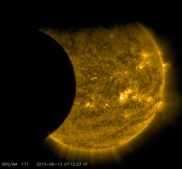 This image was taken by NASA’s Solar Dynamics Observatory at 3:12 a.m. EDT on September 13, 2015. The edge of Earth, visible near the top of the frame, appears fuzzy because Earth’s atmosphere blocks different amounts of light at different altitudes. On the left, the Moon’s edge is perfectly crisp, because it has no atmosphere. This image was taken in extreme UV wavelengths of 171 angstroms. Though this light is invisible to our eyes, it is typically colorized in gold. Image credit: NASA / SDO.
