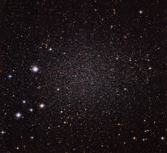 This image shows the Sculptor Dwarf Galaxy, a close neighbor of our own Milky Way Galaxy. Despite their proximity, both galaxies have very distinct histories and characters. This galaxy is much smaller, fainter and older than the Milky Way and appears here as a cloud of faint stars filling most of the image. Many other much more distant galaxies can be seen shining right through the sparse stars of the galaxy. Image credit: ESO.