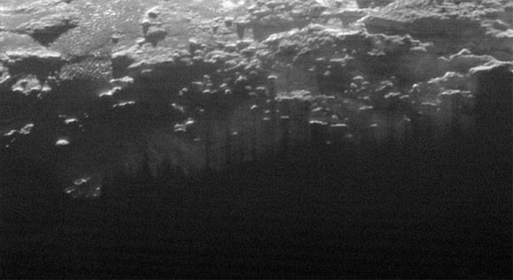 In this small section of the larger crescent image of Pluto, taken by NASA’s New Horizons just 15 minutes after the spacecraft’s closest approach on July 14, 2015, the setting Sun illuminates a fog or near-surface haze, which is cut by the parallel shadows of many local hills and small mountains. The image was taken from a distance of 11,000 miles (18,000 km), and the width of the image is 115 miles (185 km). Image credit: NASA / Johns Hopkins University Applied Physics Laboratory / Southwest Research Institute.