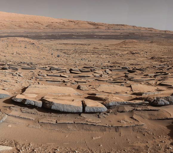 A view from the Kimberley formation looking south. The strata in the foreground dip towards the base of Mount Sharp, indicating the ancient depression that existed before the larger bulk of the mountain formed. Image credit: NASA / JPL-Caltech.