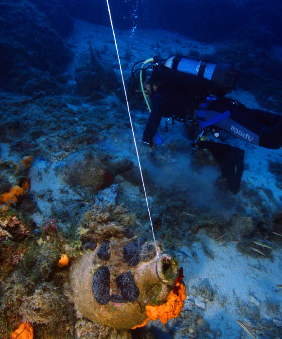 An underwater archaeologist searches around amphorae encrusted in the reef. Image credit: V. Mentogianis.