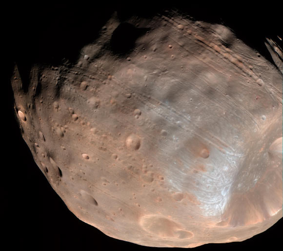 The grooves on Phobos, the larger of the two Martian moons, could be produced by tidal forces – the mutual gravitational pull of Mars and the moon. Initially, planetary scientists had thought the grooves were created by the massive impact that made Stickney crater (lower right). Image credit: NASA / JPL-Caltech / University of Arizona.