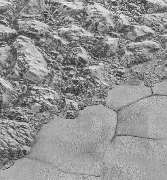 In this image of Pluto’s surface, great blocks of water-ice crust appear jammed together in al-Idrisi mountains. Some mountain sides appear coated in dark material, while other sides are bright. Several sheer faces appear to show crustal layering, perhaps related to the layers seen in some of Pluto’s crater walls. The mountains end abruptly at the shoreline of Sputnik Planum, where exotic ices of the plain form a nearly level surface, broken only by the fine trace work of striking, cellular boundaries and the textured surface of the plain’s ices. This view is about 50 miles (80.5 km) wide. The top of the image is to Pluto’s northwest. Image credit: NASA / Johns Hopkins University Applied Physics Laboratory / Southwest Research Institute.