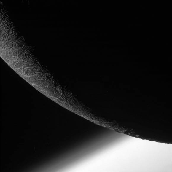 This image from Cassini shows Enceladus’ craggy, dimly lit limb, with the planet Saturn beyond. Layers can be seen in the high hazes of Saturn’s upper atmosphere, in the gradient that separates the gas giant from space. At the time of this image, the orbiter was 15,000 miles (24,000 km) from Enceladus. Image credit: NASA / JPL-Caltech / Space Science Institute.