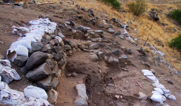 Remains of a Natufian building at NEG II: the wall of this structure is 90 cm high and is the best preserved wall excavated thus far; it is composed of 5 courses of limestone and basalt stones; the wall tilts slightly away from the structure to the northwest and two large stones mark its base at the top of the Natufian occupation level; only the western side of the structure survived, yet the contour of the curve suggests a diameter of at least 5 m. Image credit: Grosman L. et al.