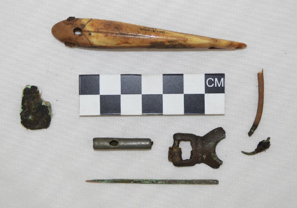 Metal and metal/ivory composite artifacts from Cape Espenberg: a bone fishing lure with iron inset eyes, a piece of bone fishing tackle with a copper hook, an eyed copper needle, a small fragment of sheet copper, a cylindrical bead and buckle fragment. Image credit: H. Kory Cooper et al.