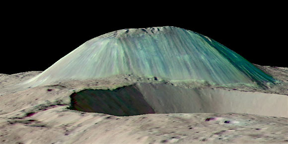Volcanic dome Ahuna Mons rises above a foreground impact crater, as seen by NASA’s Dawn spacecraft with no vertical exaggeration. Eruptions of salty, muddy water built the mountain by repeated eruptions, flows, and freezing. Streaks from falls of rocks and debris run down its flanks, while overhead views show fracturing across its summit. Image credit: Dawn Science Team / NASA / JPL-Caltech / GSFC.