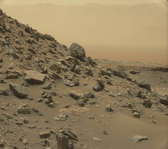 This view from Curiosity’s Mast Camera shows a sloping hillside within the ‘Murray Buttes’ region on lower Mount Sharp. The rim of Gale Crater, where the rover has been active since landing in 2012, is visible in the distance, through the dusty haze. The image was taken on September 8, 2016, during the 1454th Martian day, or sol, of Curiosity’s work on Mars. Image credit: NASA / JPL-Caltech / MSSS.