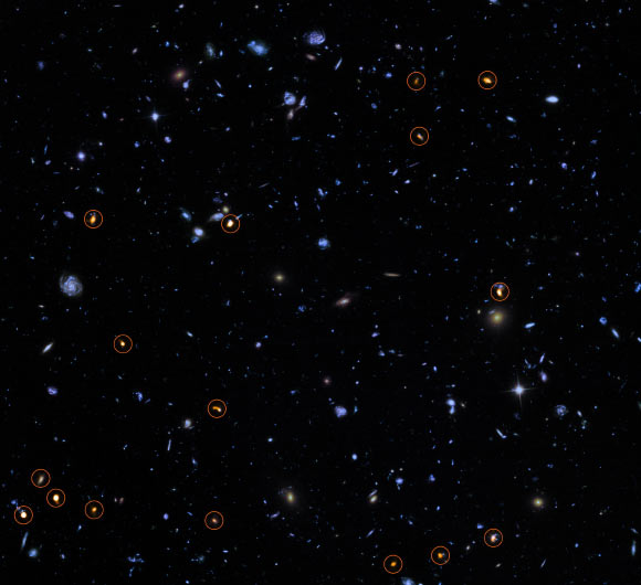 This image combines a background picture taken by Hubble (blue/green) with a new very deep ALMA view of this field (orange, marked with circles). All the objects that ALMA sees appear to be massive star-forming galaxies. Image credit: ALMA / ESO / NAOJ / NRAO / NASA / ESA / J. Dunlop et al / S. Beckwith, STScI / HUDF Team.