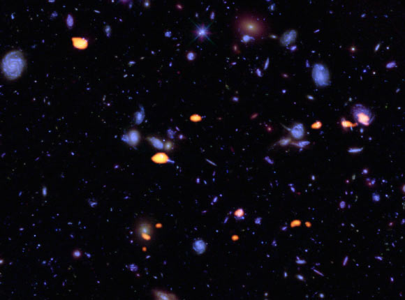 A trove of galaxies, rich in carbon monoxide (indicating star-forming potential) were imaged by ALMA (orange) in the Hubble Ultra Deep Field. The blue features are galaxies imaged by Hubble. Image credit: B. Saxton / NRAO / AUI / NSF / ALMA / ESO / NAOJ / NASA / ESA / Hubble.
