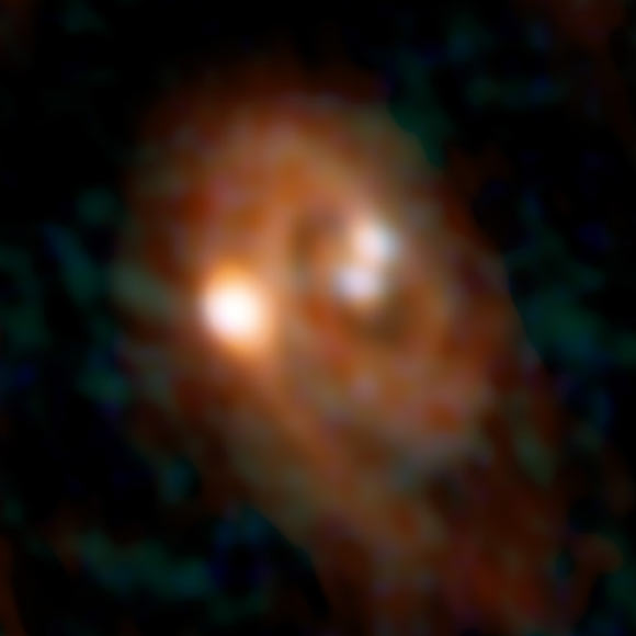 Combined ALMA and VLA image of the L1448 IRS3B system, with two young stars at the center and a third distant from them; spiral structure in the dusty disk surrounding them indicates instability in the disk. Image credit: Bill Saxton / ALMA / ESO / NAOJ / NRAO / AUI / NSF.