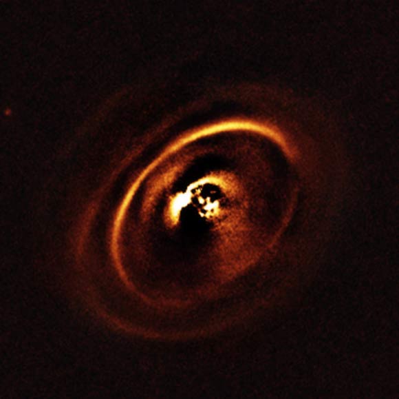 Using ESO’s SPHERE instrument, J. de Boer et al observed the planetary disk surrounding the star RX J1615 which lies in the constellation of Scorpius, 600 light-years from Earth. The observations show a complex system of concentric rings surrounding the young star, forming a shape resembling a titanic version of the rings that encircle Saturn. Such an intricate sculpting of rings in a protoplanetary disk has only been imaged a handful of times before. The central part of the image appears dark because SPHERE blocks out the light from the brilliant central star to reveal the much fainter structures surrounding it. Image credit: J. de Boer et al / ESO.