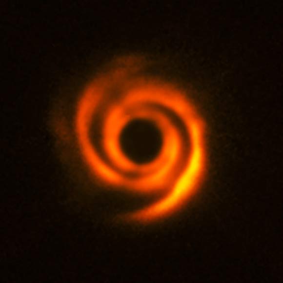 T. Stolker et al observed the planetary disk surrounding the star HD 135344B, about 450 light-years away. The disk shows prominent spiral arm-like structures. These are thought to have been created by one or multiple massive protoplanets, destined to become Jupiter-like worlds. The central part of the image appears dark because SPHERE blocks out the light from the brilliant central star to reveal the much fainter structures surrounding it. Image credit: T. Stolker et al / ESO.