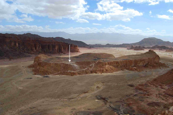 Slaves’ Hill in the center of the Timna Valley (looking east); the black slag mounds on the hilltop are visible, as well as the only access path to the site; the arrow indicates the gatehouse complex. Image credit: Erez Ben-Yosef et al.