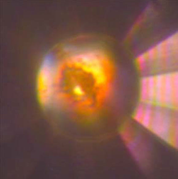 Microphotograph of the diamond anvil cell high-pressure cavity in reflected and transmitted light at 140 GPa after laser heating to > 1,500 degrees Kelvin. The sample, which consists of mixture of tI19 Na and Na2He, is in contact with He medium that is seen as a transparent area near the edge of the gasket. Image credit: Xiao Dong et al, doi: 10.1038/nchem.2716.