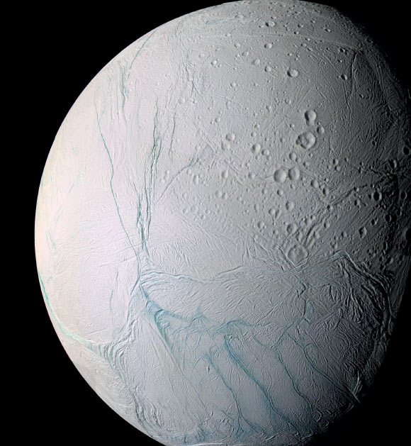 This enhanced-color view of Enceladus is largely of the southern hemisphere and includes the south polar terrain at the bottom of the image. Ancient craters remain somewhat pristine in some locales, but have clearly relaxed in others. Northward-trending fractures, likely caused by a change in the moon’s rate of rotation and the consequent flattening of the moon’s shape, rip across the southern hemisphere. The south polar terrain is marked by a striking set of ‘blue’ fractures and encircled by a conspicuous and continuous chain of folds and ridges, testament to the forces within Enceladus that have yet to be silenced. The mosaic was created from 21 false-color frames taken during Cassini’s close approaches to Enceladus on March 9 and July 14, 2005. Images taken using filters sensitive to UV, visible and IR light (spanning wavelengths from 338 to 930 nm) were combined to create the individual frames. Image credit: NASA / JPL / Space Science Institute.