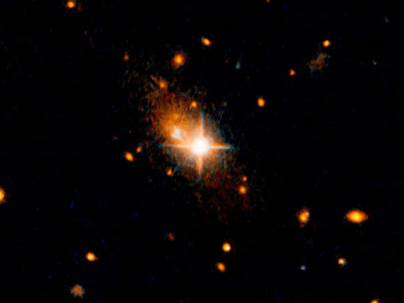 The elliptical galaxy 3C186, located about 8 billion years from Earth, is most likely the result of a merger of two galaxies. This is supported by arc-shaped tidal tails, usually produced by a gravitational tug between two colliding galaxies, identified by M. Chiaberge et al. The merger of the galaxies also led to a merger of the two supermassive black holes in their centers, and the resultant black hole was then kicked out of its parent galaxy by the gravitational waves created by the merger. The bright, star-like looking quasar can be seen in the center of the image. Its former host galaxy is the faint, extended object behind it. Image credit: NASA / ESA / M. Chiaberge, STScI.
