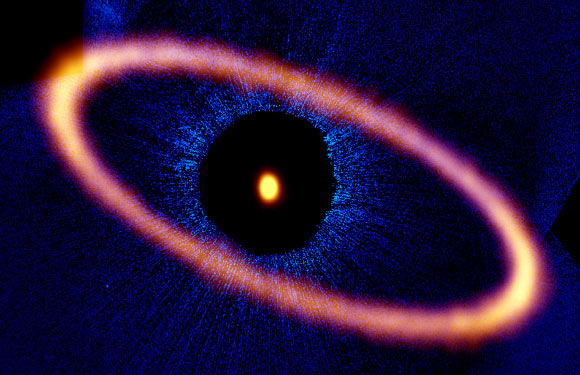 Composite image of the Fomalhaut star system. The ALMA data, shown in orange, reveal the distant and eccentric debris disk in never-before-seen detail. The central dot is the unresolved emission from the star, which is about twice the mass of our Sun. Optical data from the NASA/ESA Hubble Space Telescope is in blue; the dark region is a coronagraphic mask, which filtered out the otherwise overwhelming light of the central star. Image credit: ALMA / ESO / NAOJ / NRAO / M. MacGregor / NASA / ESA / Hubble / P. Kalas / B. Saxton / AUI / NSF.