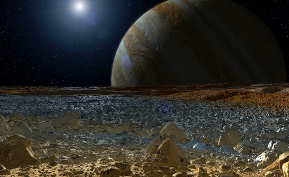 This artist’s concept shows a simulated view from the surface of Jupiters moon Europa. Europa’s potentially rough, icy surface, tinged with reddish areas, can be seen in the foreground. The giant planet Jupiter looms over the horizon. Image credit: NASA / JPL-Caltech.