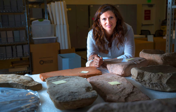 Dr. Louderback stands behind large stone metates, the grindstones on which ancient Native Americans processed their food. Image credit: University of Utah.