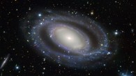 This image shows the barred-ring spiral galaxy NGC 7098 (center). An array of distant galaxies are also visible throughout the frame, the most prominent being the small, edge-on, spiral galaxy visible to the left of NGC 7098, known as ESO 048-G007. Image credit: ESO.
