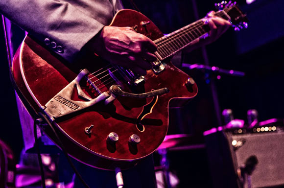 Musician on stage playing an electric guitar. Image credit: Herb1979.