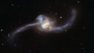 NGC 2623 is in the late stages of the merging process, with the centers of the original galaxy pair now merged into one nucleus, but stretching out from the center are two tidal tails of young stars, a strong indicator that a merger has taken place. During such a collision, the dramatic exchange of mass and gases initiates star formation, seen here in both the tails. The prominent lower tail is richly populated with bright star clusters. These star clusters may have formed as part of a loop of stretched material associated with the northern tail, or they may have formed from debris falling back onto the nucleus. In addition to this active star-forming region, both galactic arms harbor very young stars in the early stages of their evolutionary journey. Image credit: NASA / ESA / Hubble.