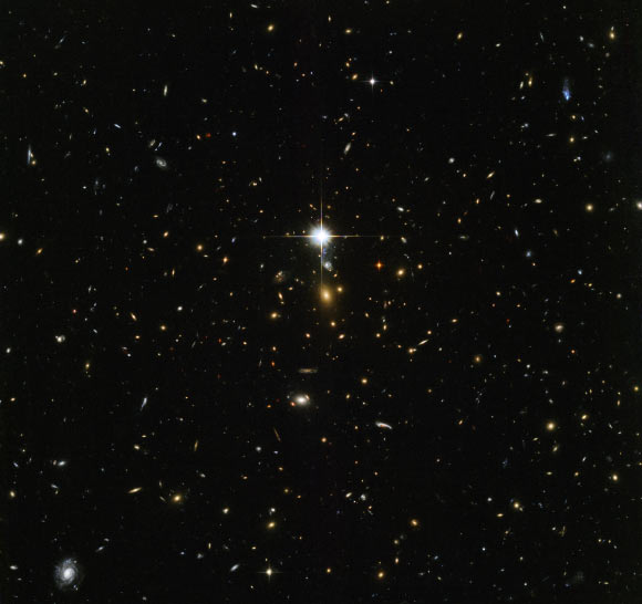 This Hubble image shows the massive galaxy cluster WHL J24.3324-8.477. The bright flash in the middle of the image is actually a star lying within our Milky Way Galaxy. Image credit: NASA / ESA / Hubble.