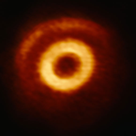 This image from the Atacama Large Millimeter/submillimeter Array shows a central ring of matter and a crescent structure within the circumstellar disk around V1247 Orionis. Image credit: ALMA / ESO / NAOJ / NRAO / S. Kraus, University of Exeter.