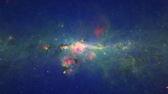 The region around the center of our Milky Way Galaxy glows colorfully in this image taken by NASA’s Spitzer Space Telescope. In the image, the myriad of stars crowding the center of our Galaxy creates the blue haze that brightens towards the center of the image. The green features are from carbon-rich dust molecules, called polycyclic aromatic hydrocarbons, which are illuminated by the surrounding starlight as they swirl around the Galaxy’s core. The yellow-red patches are the thermal glow from warm dust. The polycyclic aromatic hydrocarbons and dust are associated with bustling hubs of young stars. These materials, mixed with gas, are required for making new stars. The brightest white feature at the center of the image is the central star cluster in our Galaxy. At a distance of 26,000 light years away from Earth, it is so distant that, to Spitzer’s view, most of the light from the thousands of individual stars is blurred into a single glowing blotch. The region pictured here is immense, with a horizontal span of 2,400 light-years (5.3 degrees) and a vertical span of 1,360 light-years (3 degrees). Though most of the objects seen in this image are located near the Galactic center, the features above and below the Galactic plane tend to lie closer to Earth. Image credit: NASA / JPL-Caltech.