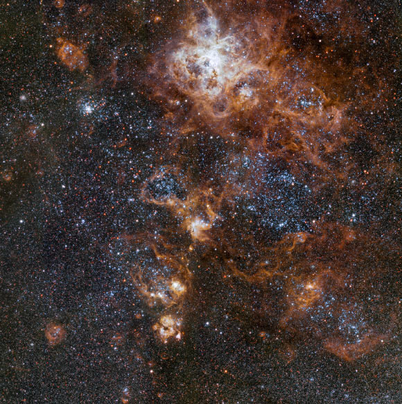 This image from the 256-megapixel OmegaCAM camera on ESO’s VLT Survey Telescope shows the Tarantula Nebula and its rich surroundings in great detail. It reveals a cosmic landscape of star clusters, glowing gas clouds and the scattered remains of supernova explosions. Image credit: ESO.