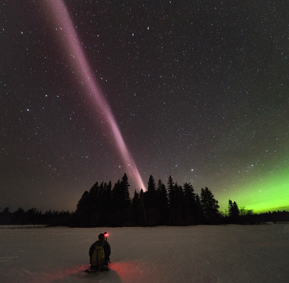 Alberta Aurora Chasers capture STEVE on the evening of April 10, 2018 in Prince George, British Columbia, Canada. Fellow Aurora Chaser Robert Downie kneels in the foreground while photographer Ryan Sault captures the narrow ribbon of white-purple hues overhead. The vibrant green aurora is seen in the distant north, located to the right in the photo. Image credit: Ryan Sault.