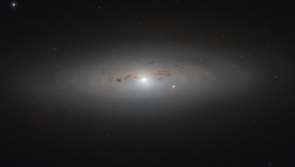 This Hubble image shows the lenticular galaxy NGC 4036. The bright star visible slightly to the right of the galactic center is not within the galaxy itself; it sits between us and NGC 4036, adding a burst of brightness to the scene. The image is a composite of separate exposures acquired by Hubble’s Advanced Camera for Surveys (ACS) instrument. Two filters were used to sample various wavelengths. The color results from assigning different hues to each monochromatic image associated with an individual filter. Image credit: NASA / ESA / Hubble / Judy Schmidt, www.geckzilla.com.